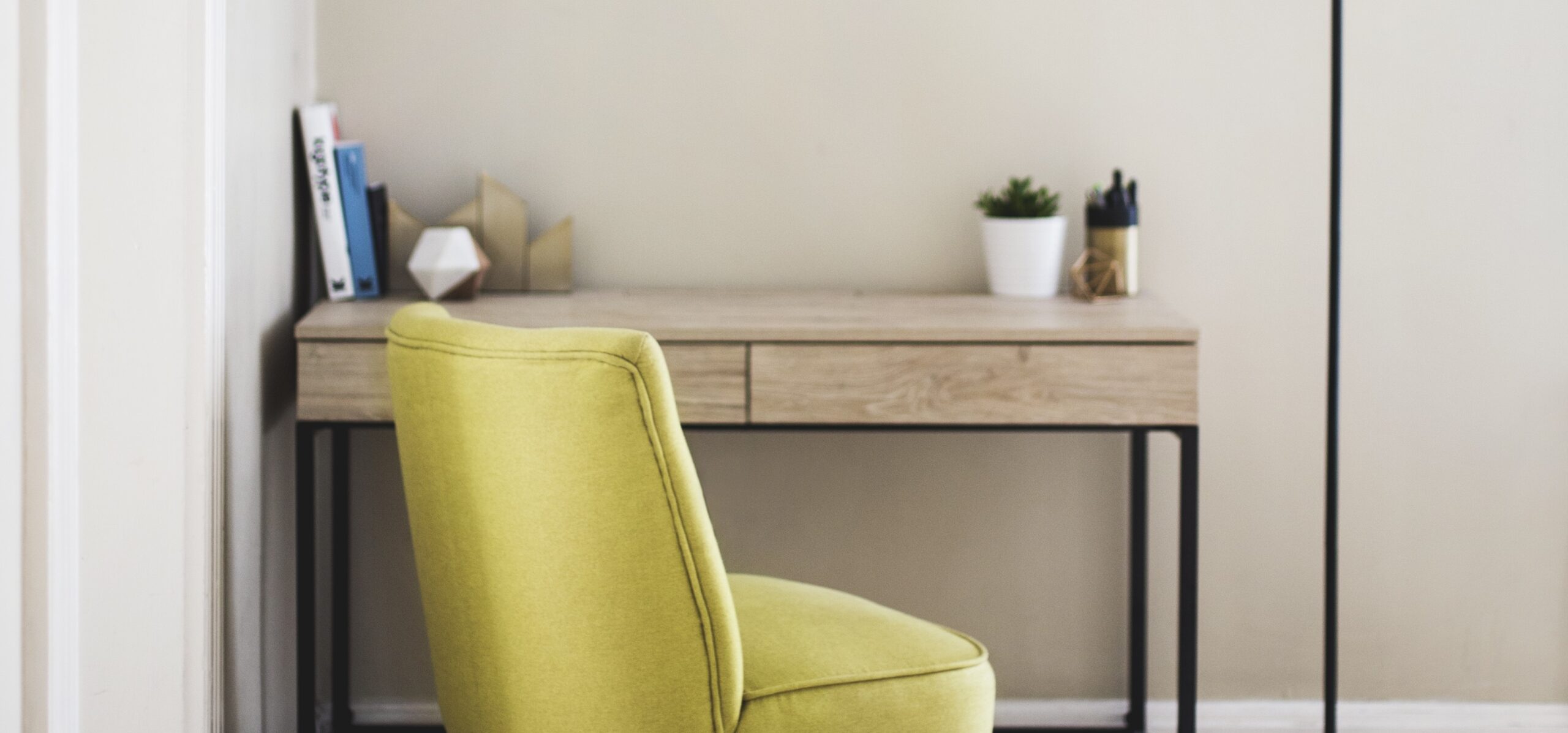 Vertical shot of a yellow chair and tall lamp near a wooden table with books and plant pots on it